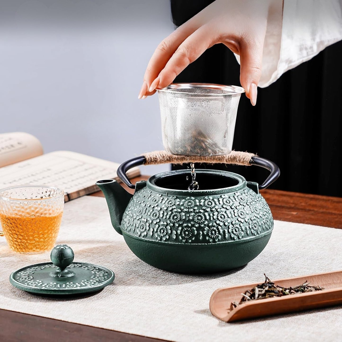 theiere en fonte verte sur table avec tasse the infuseur tenue par femme