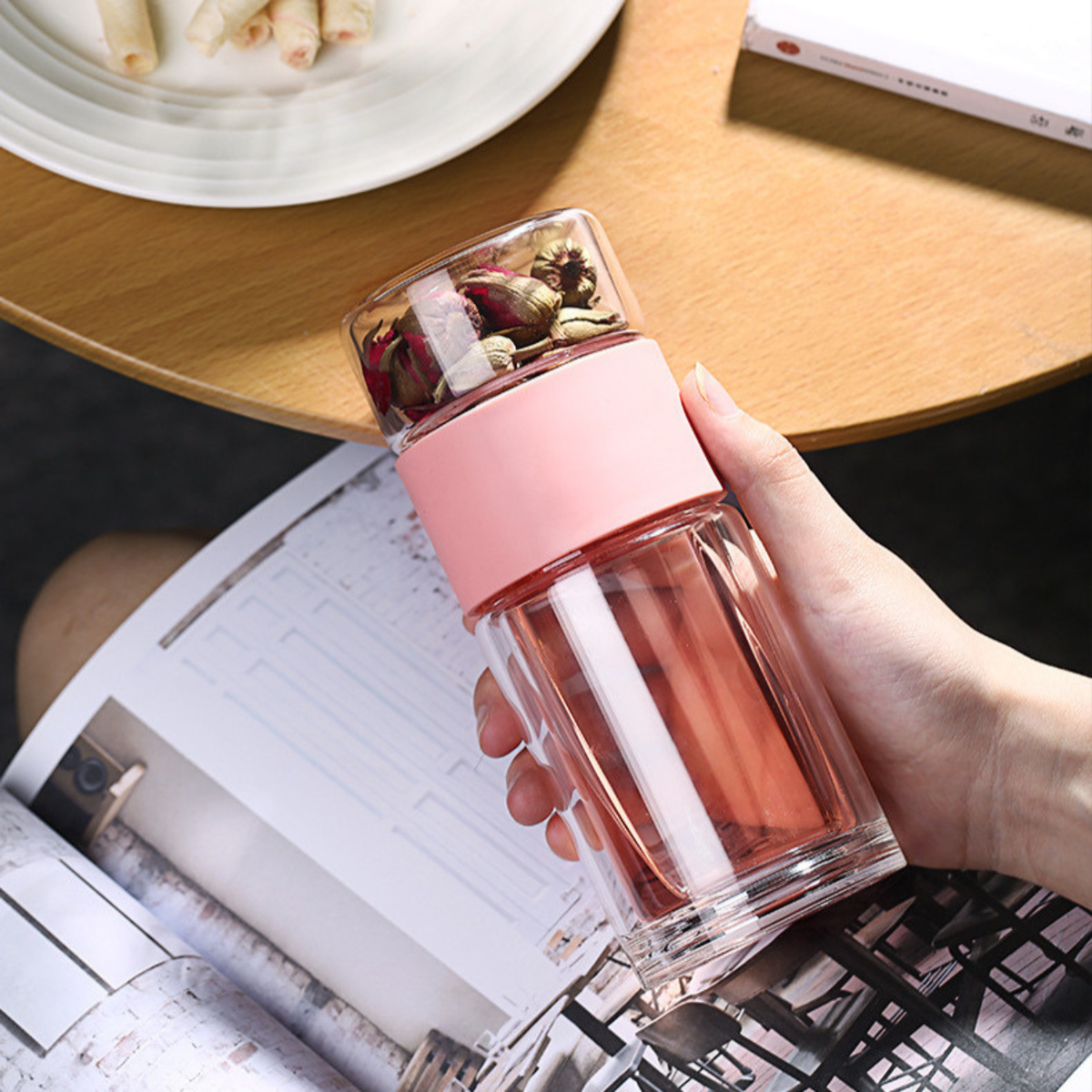bouteille théière en verre rose tenue par une femme lisant livre