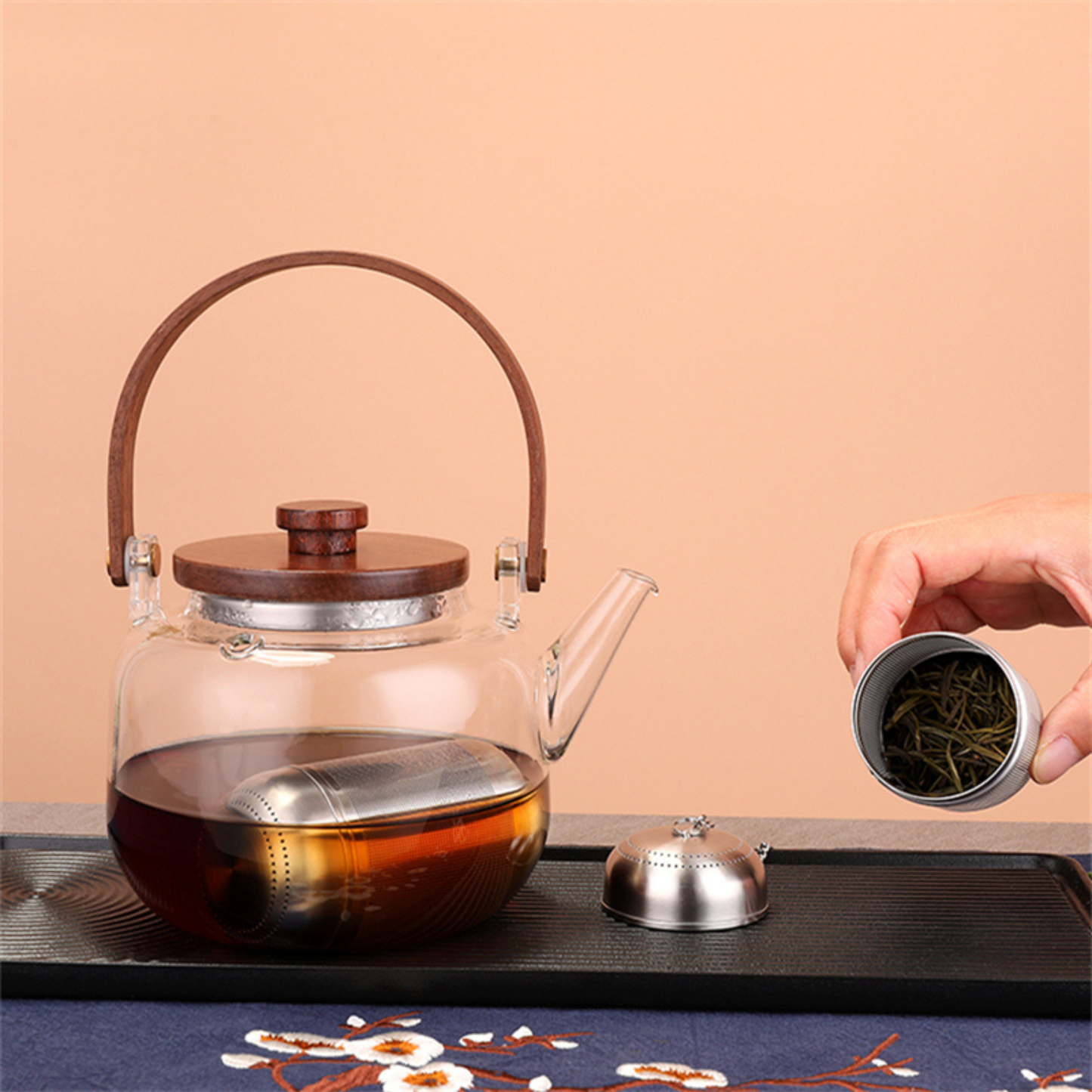 infuseur a the dans theiere sur plateau personne a cote montrant infuseur remplit de the