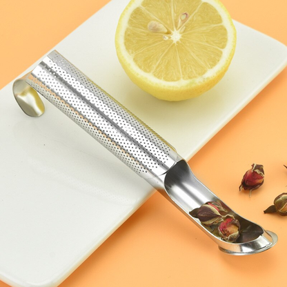 infuseur thé ouvert avec des fleuilles de the séché sur planche blanche citron à coté