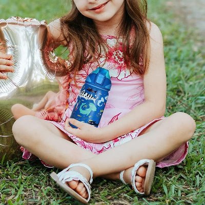 jeune fille tenant gourde isotherme bleu avec motif requin assise sur gazon
