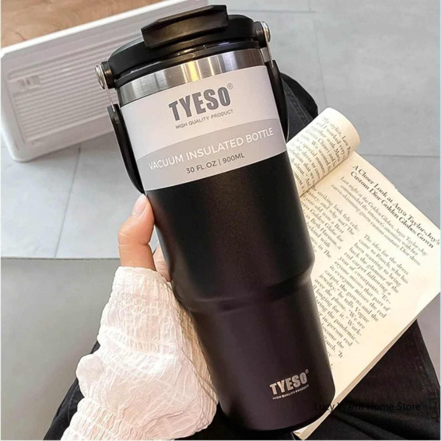 mug isotherme de voyage noire tenue par une femme avec son livre a cote