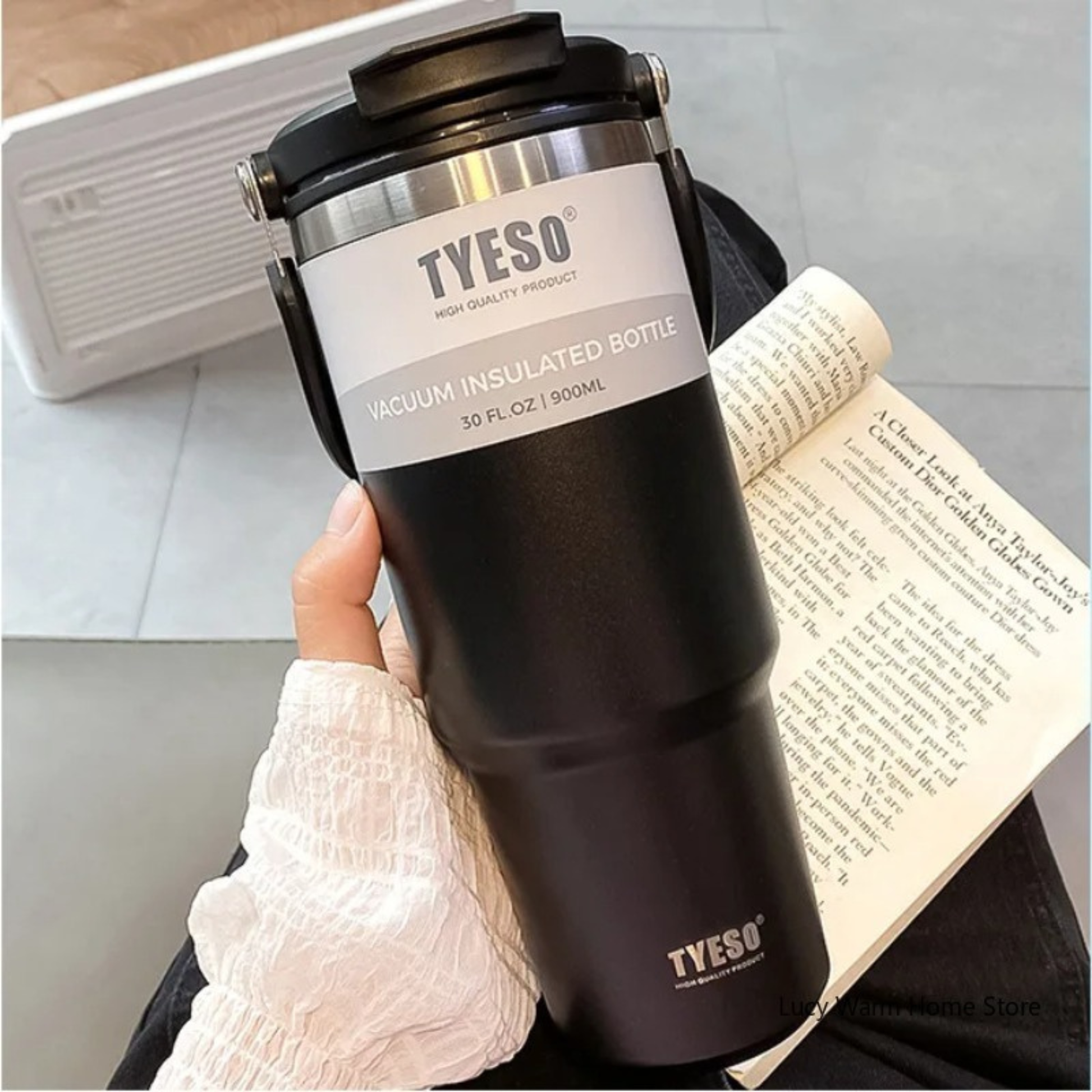 mug isotherme de voyage noire tenue par une femme avec son livre a cote