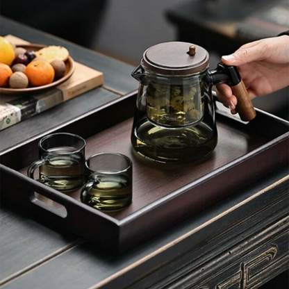 théière en verre et bois tenue par personne sur plateau bois